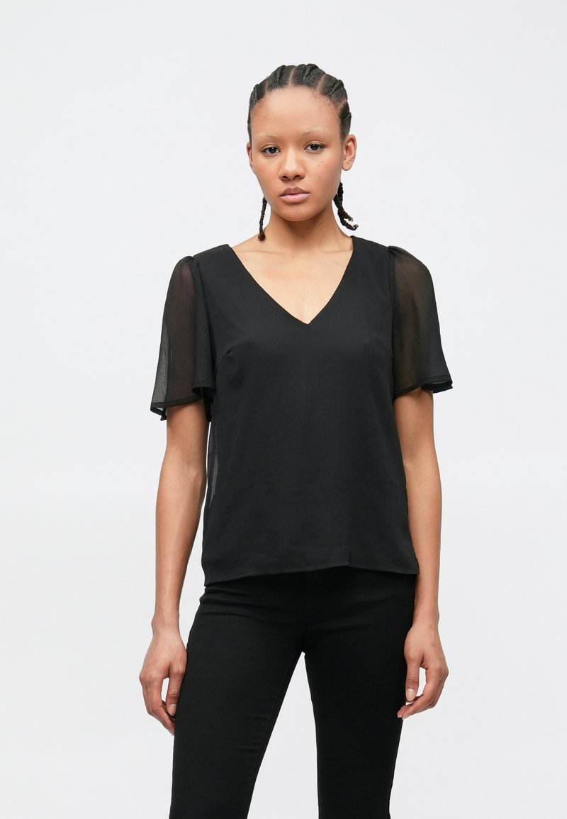 Μαύρη μπλούζα με V λαιμόκοψη, κοντά διάφανα μανίκια και άνετη γραμμή. Το ύφασμα έχει ομαλή υφή και είναι ελαφρύ, κατάλληλο για στιλιστικές στρώσεις.