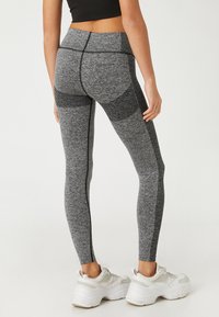 Leggings de sport gris avec des panneaux texturés, taille haute et coutures contrastantes. Associés à des baskets blanches sportives à semelles épaisses.