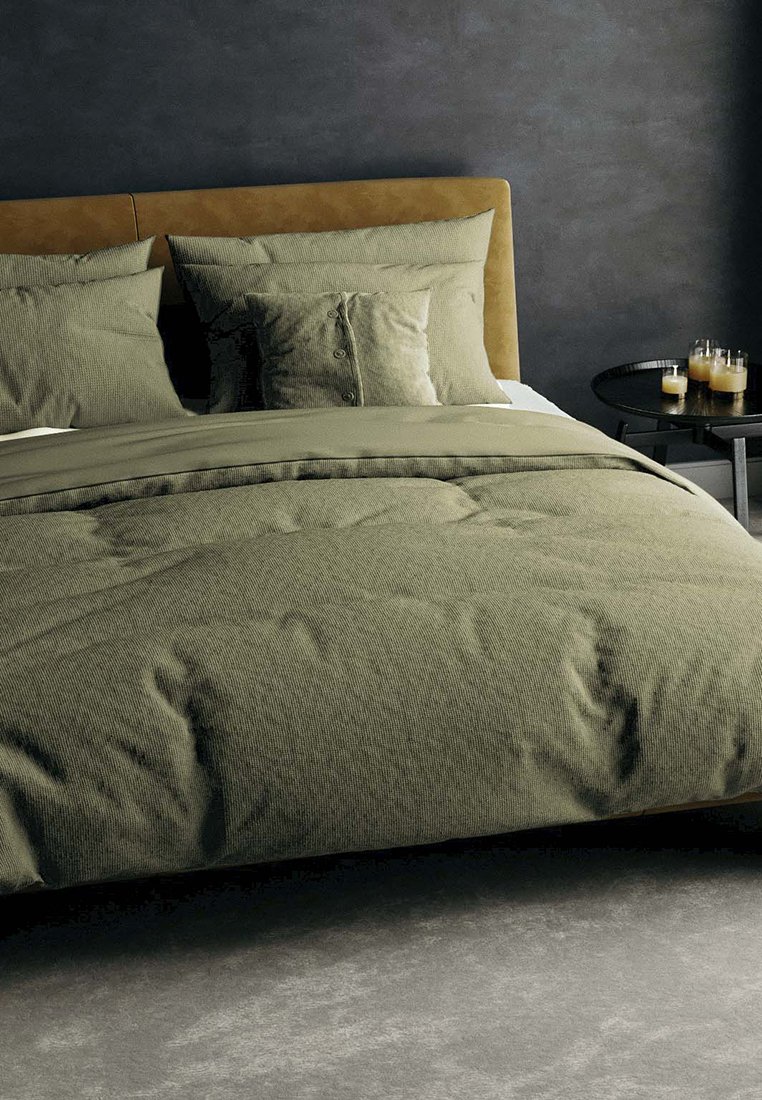 Olivgrünes Bettwäsche-Set mit strukturiertem Bettdeckenbezug und Kissen, das über Knopfakzente verfügt. Weicher, knitterfreier Stoff auf einem Bett mit einem braunen gepolsterten Kopfteil.