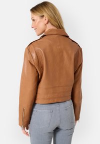 Braune Leder-Bomberjacke mit strukturiertem Design, featuring Schulterdetails und Reißverschlüssen an den Ärmelbündchen. Weiche Textur mit glatter Oberfläche.