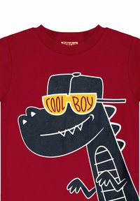 Rotes Baumwoll-T-Shirt mit einem cartoonhaften Dinosaurier in Schwarz, der gelbe Sonnenbrillen trägt, und dem Text "COOL BOY", akzentuiert mit weißen Umrandungen.