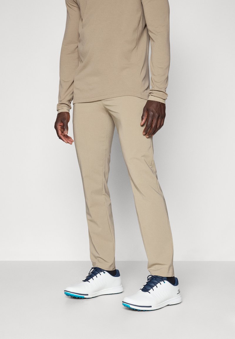 Beige long-sleeve shirt and matching slim-fit pants made of a soft material, paired with white and navy athletic shoes.