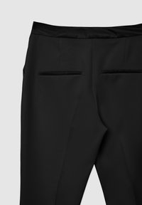 Pantalons noirs à la finition lisse, dotés d'une ceinture satinée et de deux poches arrière. Forme ajustée avec des lignes épurées.