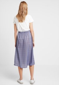 Gonna midi blu e bianca a motivo con vita elastica arricciata, silhouette fluida, indossata con una t-shirt bianca e sneakers bianche.