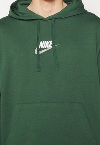 Grön bomullshuvtröja med en framficka, dragsko i huvan och en vit Nike-logotyp broderad på bröstet.