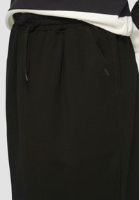 Pantaloni neri in tessuto liscio, caratterizzati da una vita elastica con cordoncino e tasche laterali per funzionalità.