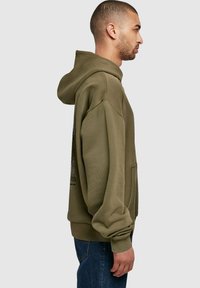 Sweat-shirt à capuche vert olive au design décontracté, avec des poignets côtelés et une poche. Présente un imprimé graphique sur le devant.