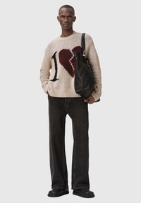 Πλεκτό πουλόβερ σε μπεζ με μεγάλο μαύρο "1" και σχέδιο κόκκινης καρδιάς. Συνδυάζεται με σκούρο παντελόνι φαρδιάς γραμμής και μαύρη χαλαρή τσάντα. Μαύρα παπούτσια.