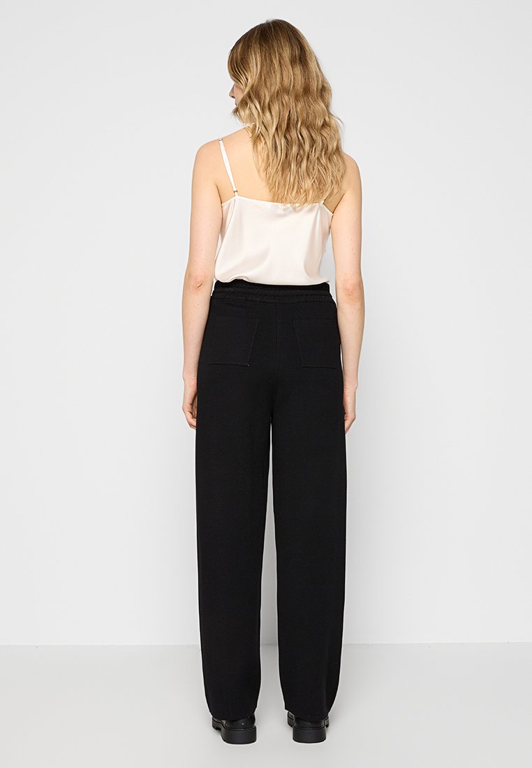 Schwarz weit geschnittene Hose mit elastischem Bund, zwei Gesäßtaschen und glatter Stoffstruktur, kombiniert mit einem hellen Satin-Top.