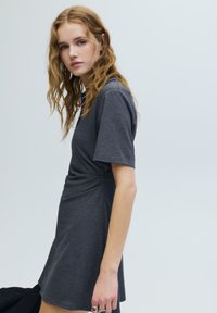 Szürke, rövid ujjú ruha, amelyen csavart derékrész található, puha, texturált anyagból készült. Egyszerű kialakítás, enyhén bővülő szegéllyel.