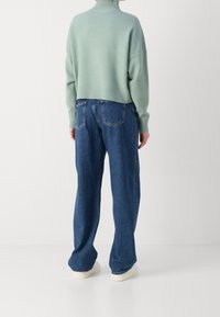 Pull court vert menthe avec ourlet côtelé et col montant associé à un jean en denim bleu ample. Des baskets blanches complètent l'ensemble.