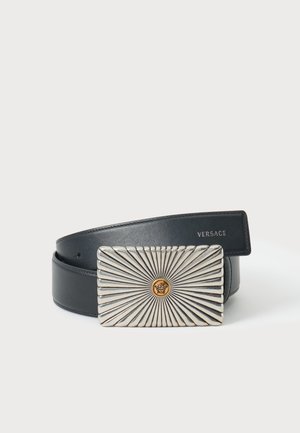 Zwarte leren riem met een rechthoekige zilveren gesp met uitstralende lijnen en een klein gouden Medusa-hoofd embleem in het midden.
