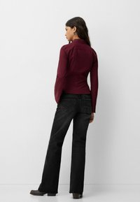 Burgundy anpassad långärmad skjorta med spetsig krage, matchad med svarta vida jeans. Klädseln har subtila sömnadsdetaljer.