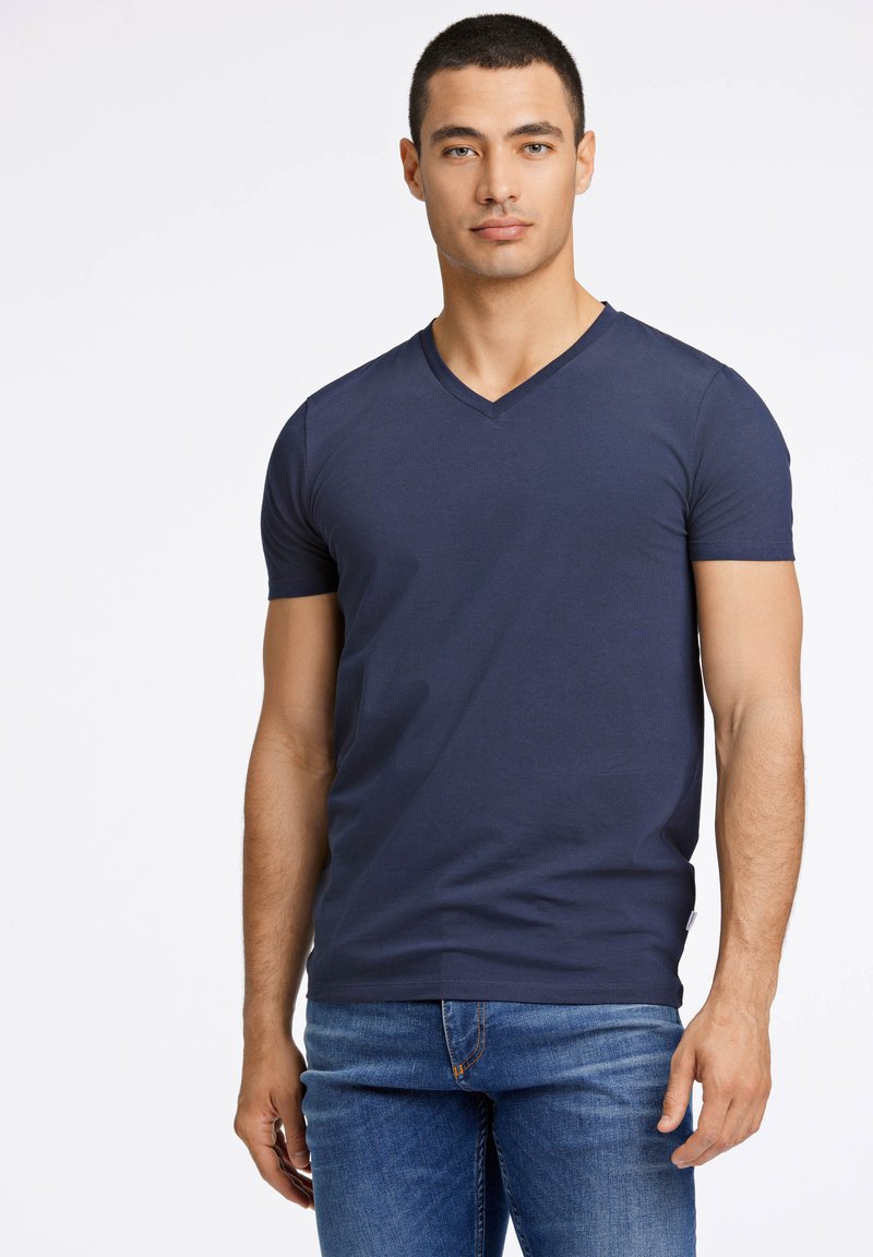 Marineblaues V-Ausschnitt-T-Shirt aus Baumwolle, mit kurzen Ärmeln und tailliertem Design, kombiniert mit Jeans.