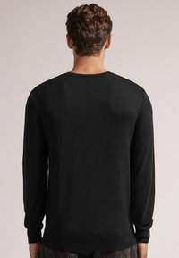 Svart långärmad tröja, rundad hals, tillverkad av texturerat stickat tyg, med ribbade manschetter och nederkant. Visningen visar baksidan.
