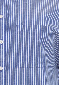 Camicia a righe blu e bianche realizzata in tessuto leggero, con chiusura a bottoni e taschino applicato sul lato sinistro.
