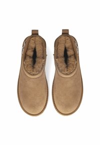 Botas marrones de tobillo hechas de suave ante con forro de piel sintética, que cuentan con una textura lisa y una suela cosida. Dos acentos en las lengüetas traseras.