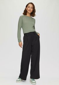 Haut à manches longues côtelé vert associé à un pantalon large à taille haute noir avec des accents de boutons et des baskets vertes.