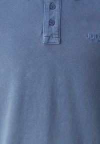 Modra polo majica iz teksturiranega materiala, z dvema gumboma na izrezu in diskretno izvezenim logotipom na prsih.