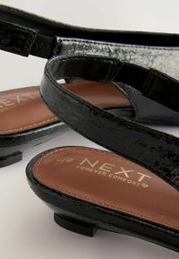 Svarta sandaler med texturerade remmar, bruna vadderade innersulor och små klackar. Har tryckt logotyp "NEXT FOREVER COMFORT" på innersulorna.