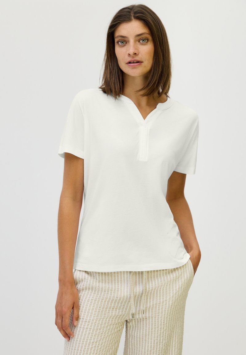 Haut à manches courtes blanc avec un décolleté en V et une coupe décontractée. Le tissu semble lisse et léger, adapté à un usage décontracté.