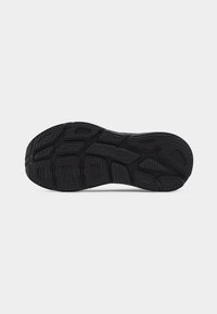 Semelle de chaussure en caoutchouc noir avec des motifs de crampons profonds et le logo "HOKA" visible au centre, présentée sur un fond clair uni.