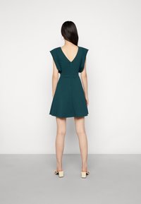 Tyrkysové šaty s V-výstřihem, krátkými rukávy a rozšířenou sukní. Vyrobeny z hladkého materiálu, mají zipový uzávěr na zádech. Jednoduchý a strukturovaný design.