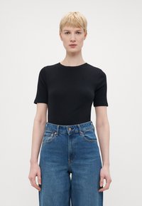 Svart kortermet t-skjorte med rund hals, sammen med høyt liv blå denim jeans med en klassisk fem-lomme-design.