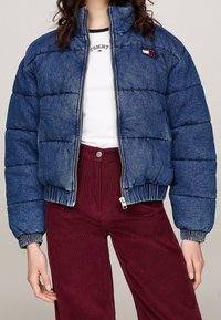 Džínová péřová bunda modré barvy, prošívaný design, vysoký límec, přední zip a elastické manžety, spárovaná s bordó kordovým kalhotami.
