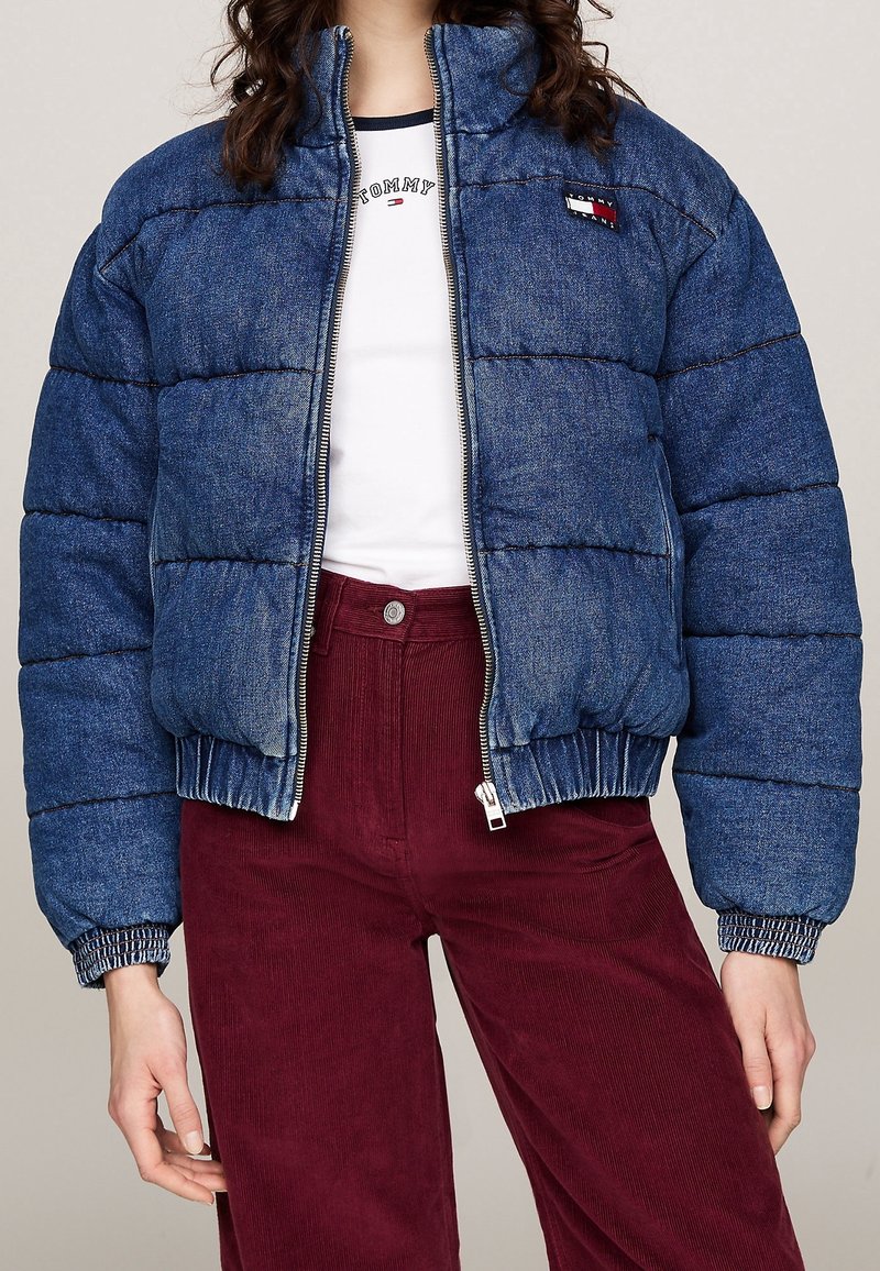 Džínová péřová bunda modré barvy, prošívaný design, vysoký límec, přední zip a elastické manžety, spárovaná s bordó kordovým kalhotami.