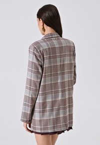 Geruite blazer in grijs en bordeaux, met een getailleerde pasvorm, enkelvoudige knoopsluiting en subtiele branding op de kraag.