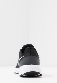 Scarpa da ginnastica nera con una texture liscia, dotata di dettagli grigi e suola in gomma bianca. La vista posteriore mette in evidenza un design snello.