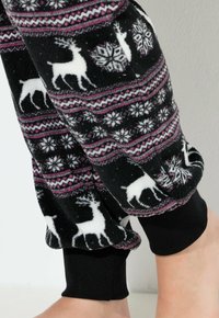 Pantalones de lounge de forro polar negro con una textura suave, patrones de renos en rosa y blanco, copos de nieve y puños negros en los tobillos.