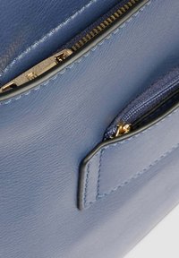 Primer plano de un bolso de cuero azul que muestra dos compartimentos con cremallera con cierres metálicos en tono dorado y bordes cosidos.