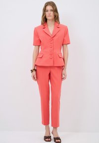 Coral tailored blazer with short sleeves and six buttons, paired with matching slim-fit trousers. Soft texture, minimalistic design.