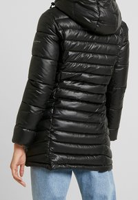 Černá prošívaná bunda s kapucí a elastickými manžetami. Disponuje hladkým, lesklým povrchem a přiléhavým střihem.