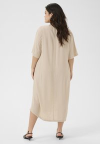 Beige, knälång klänning med korta ärmar och avslappnad passform. Slät tyg med en subtil glans. Viser en enkel, minimalistisk design.