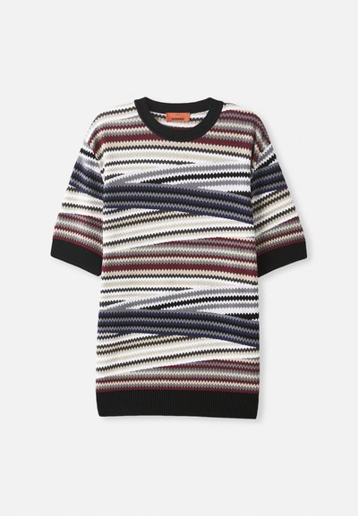 Adītu īsām piedurknēm džemperis ar daudzkrāsainu zīgzaga rakstu sarkanā, zilā, baltā un melnā krāsā, ar ribotu melnu apkakli un piedurknēm.