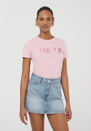 T-shirt in cotone rosa con la scritta "AMOUR" stampata in lettere lucide, abbinata a una mini gonna in denim azzurro chiaro con un design classico a cinque tasche.