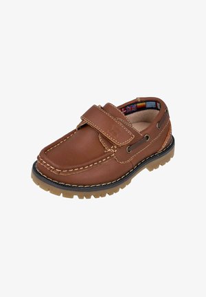 Zapato de cuero marrón con punta redonda, correa de Velcro, costura texturizada y suela de goma flexible. El interior presenta un patrón de banderas coloridas.