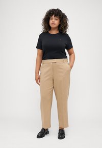 Svart t-skjorte med korte ermer kombinert med beige bukser med høy midje. Buksene har rette ben, sidelommer og en glatt tekstur. Sorte loafers.
