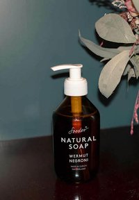 Bottiglia in vetro ambra con pompa di sapone naturale etichettata "Wermut Negroni", con parte superiore della pompa bianca, testo nero, design minimalista, poggiata su uno sfondo scuro.