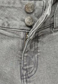 Sive traperice s srebrnim detaljima, uključujući dvije tipke na druker i zip zatvarač, s mekim, teksturiranim završetkom i detaljem na stražnjem džepu.
