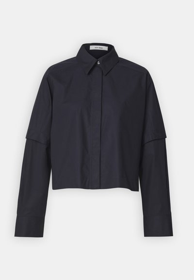Camicia di colore blu scuro, tagliata, con colletto classico, maniche lunghe e chiusura a bottoni. Presenta spalle strutturate e una texture del tessuto liscia.