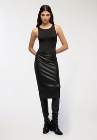 Czarny bezrękawnik w połączeniu z czarną skórzaną spódnicą o średniej długości z bocznym rozcięciem, uzupełnioną czarnymi kozakami do kolan.