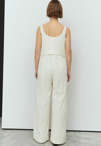 Jumpsuit blanc sans manches avec un top court et un pantalon évasé. Tissu texturé avec un léger éclat. Design simple et épuré sans embellissements.