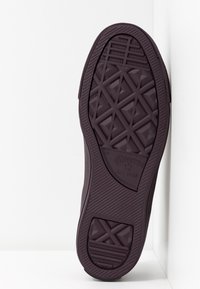 Mörklila gummisula med en texturerad diamantmönster, med "Converse All Star"-logotypen och ribbade kanter för grepp.