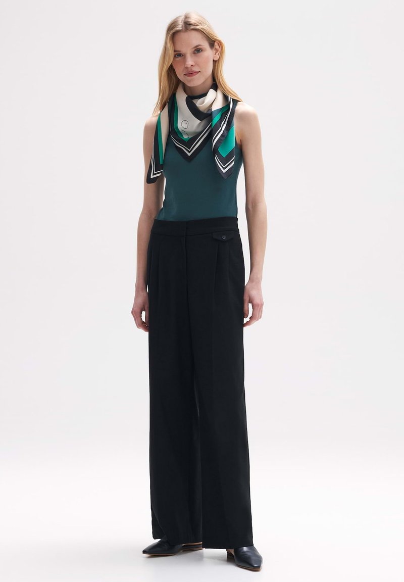 Zwarte wijde broek met een hoge taille, gecombineerd met een teal mouwloos top en een meerkleurige zijden sjaal met geometrische patronen.