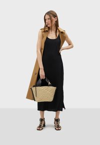 Crna plisirana midi haljina s bež bezrukavim trench kaputom, wovena torba od trske i crne sandale sa potpeticom ukrašene zlatnim studovima.