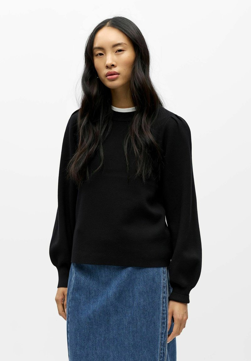 Pull noir en tricot avec des manches longues et volumineuses et un col rond, associé à une jupe en jean bleu clair. Texture lisse.